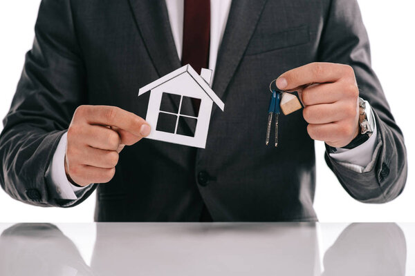 cropped view of mortgage broker holding paper house and keys isolated on white