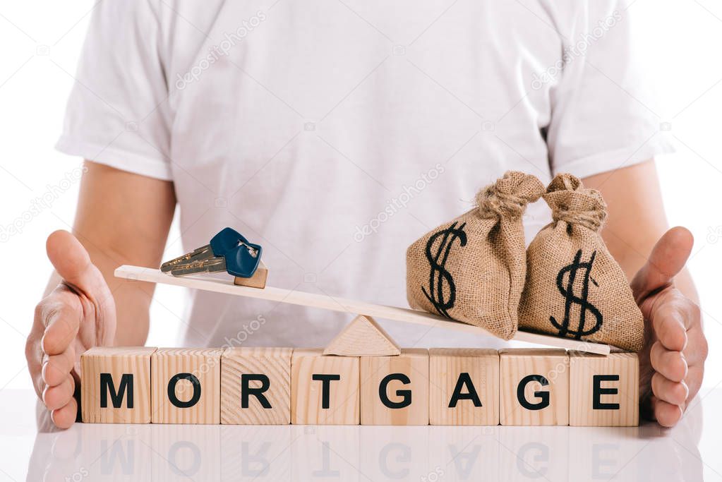 cropped view of man holding scales with moneybags and keys on cubes with mortgage lettering isolated on white