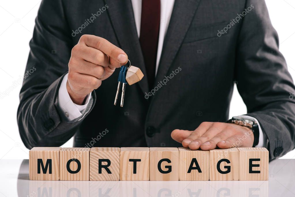 cropped view of businessman holding keys near wooden cubes with mortgage lettering isolated on white