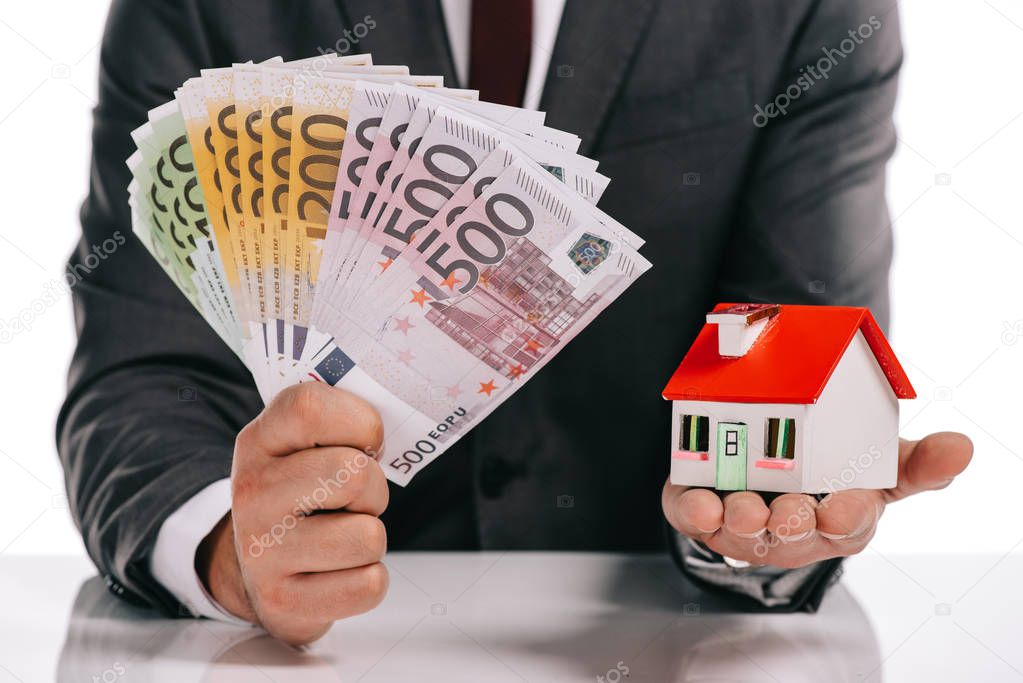 cropped view of businessman holding house model and euro banknotes isolated on white, mortgage concept