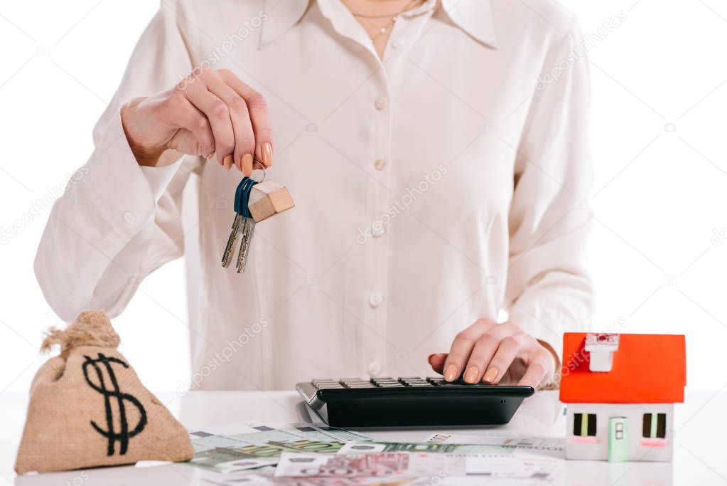 cropped view of businesswoman holding keys and using calculator isolated on white, mortgage concept
