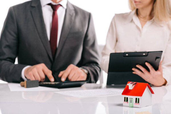 selective focus of house model with businesspeople with calculator and clipboard isolated on white,  mortgage concept