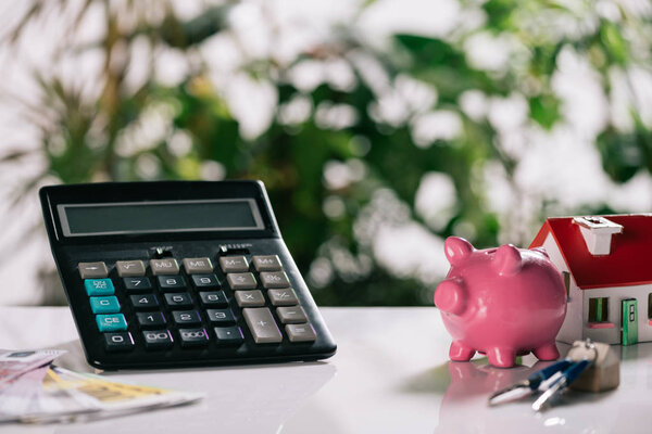 selective focus of euro banknotes, keys, piggy bank, calculator and house model on white desk, mortgage concept