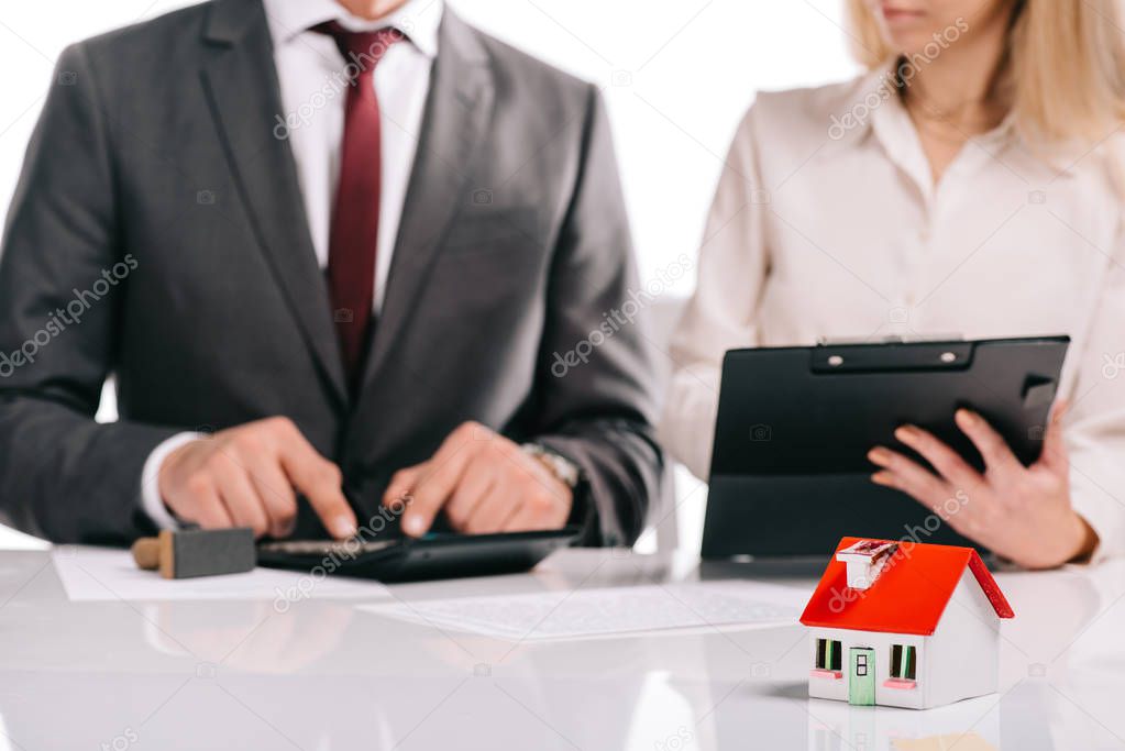 selective focus of house model with businesspeople with calculator and clipboard isolated on white,  mortgage concept