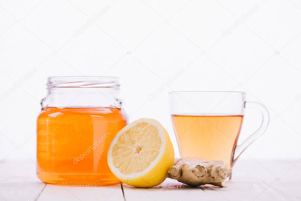 tea with lemon and ginger root in jar and glass cup on wooden table isolated on white