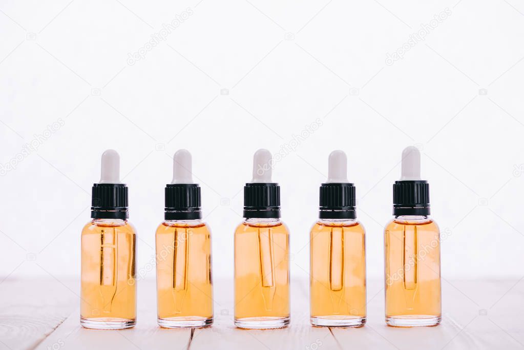 row of cbd oil in bottles with droppers on wooden surface isolated on white