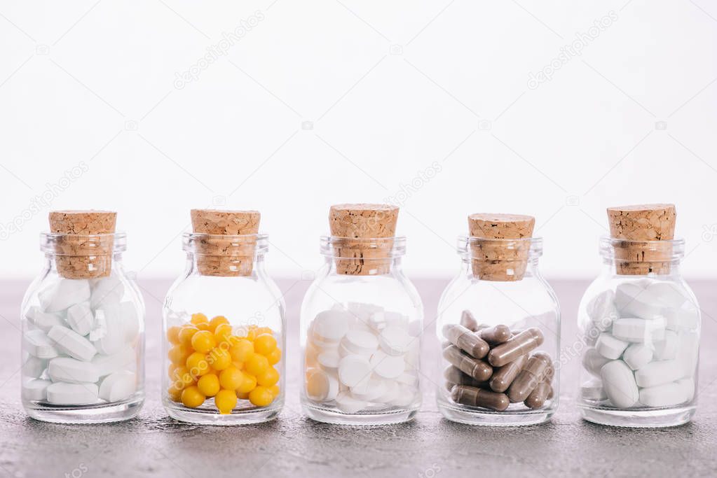 row of bottles with corks and different pills isolated on white