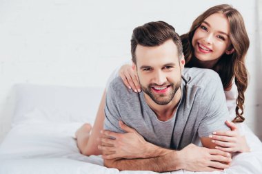 Genç sevgili çift gülümseyen ve beyaz yatak üzerinde yalan