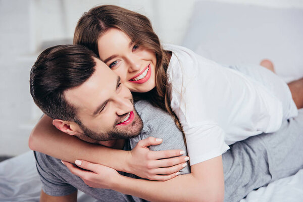 selective focus of young loving couple hugging and smiling in bed