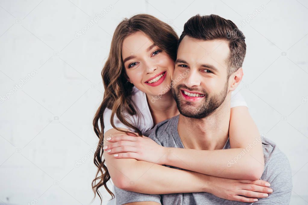 selective focus of happy couple embracing and smiling in white bedroom
