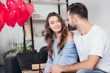 mutlu adam oda kalp şeklinde balonlarla süslenmiş kadında bakarak