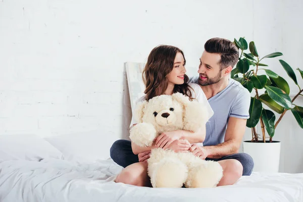 Happy Couple Embracing Teddy Bear While Sitting Bed White Bedding — Stock Photo, Image