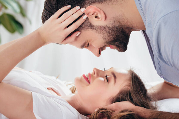 selective focus of young loving man and woman gentle embracing and looking into eyes in bed 
