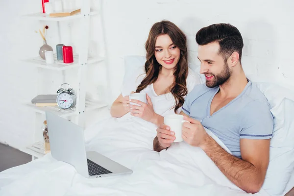 Young Couple Holding Cups Lying Bed Watching Movie Laptop — Stock Photo, Image