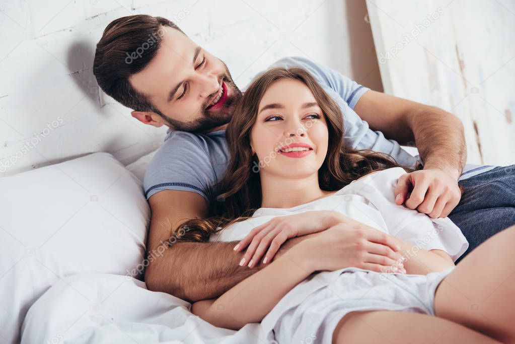 young adult loving couple smiling and gentle embracing in bed 