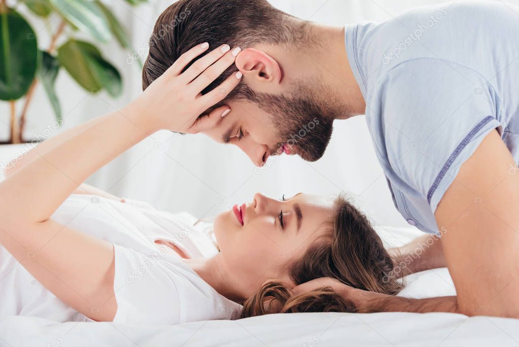 selective focus of young loving couple gentle embracing and looking into eyes in bed 