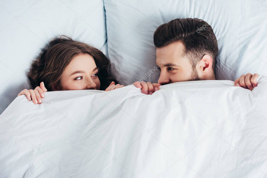 young loving couple hiding under blanket in bed and looking into eyes