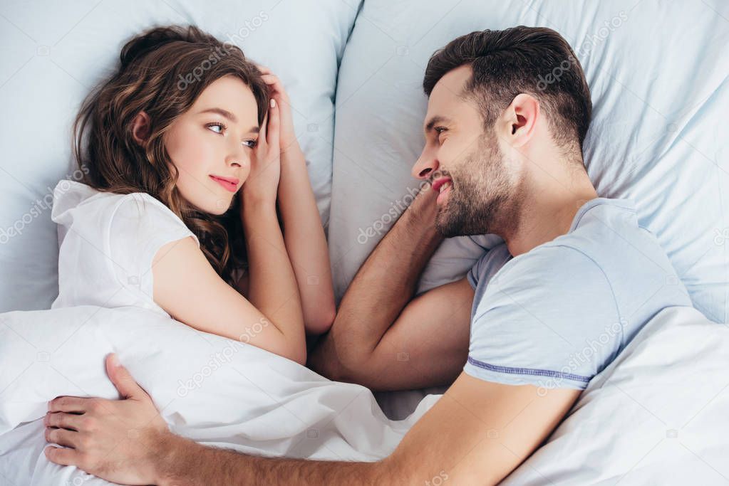 young loving boyfriend gentle embracing girlfriend in bed and looking in eyes