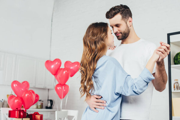 happy couple dancing at home in room decorated with heart-shaped balloons 