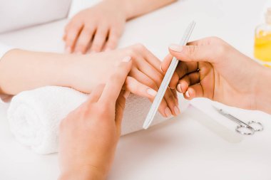 Cropped view of woman holding hand on towel while manicurist filing nails clipart