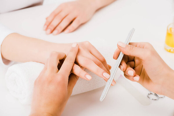 Partial view of manicurist holding fingers while doing nail form