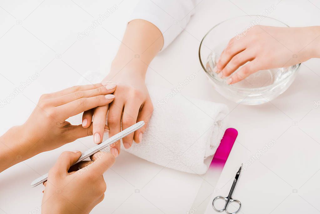 Partial view of manicurist holding fingers and making nail form 
