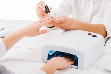Kısmi manikürcü çivi lamba kullanarak müşteri ise tırnak cilası uygulayarak görünümünü