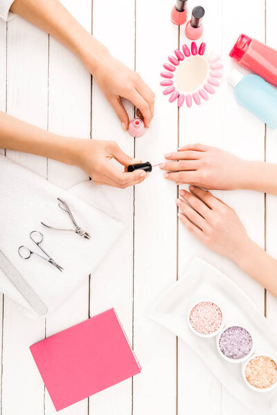 Top view of manicurist applying pink nail polish