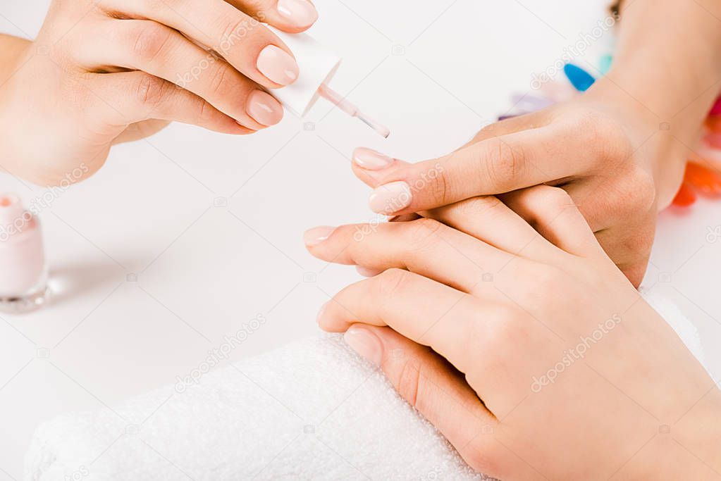 Partial view of manicurist gently holding hand while applying nail polish