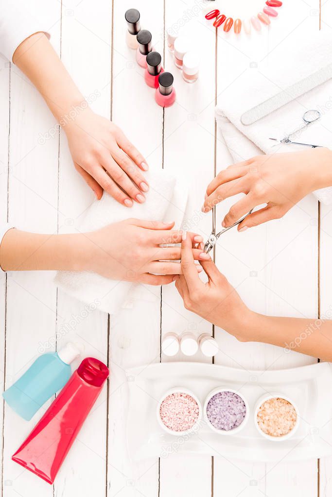 Partial view of manicurist using nail clippers while working with customer