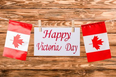 top view of canadian flags and card with 'happy victoria day' lettering on wooden background clipart