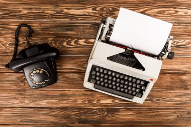 top view of typewriter and rotary dial telephone on wooden table clipart