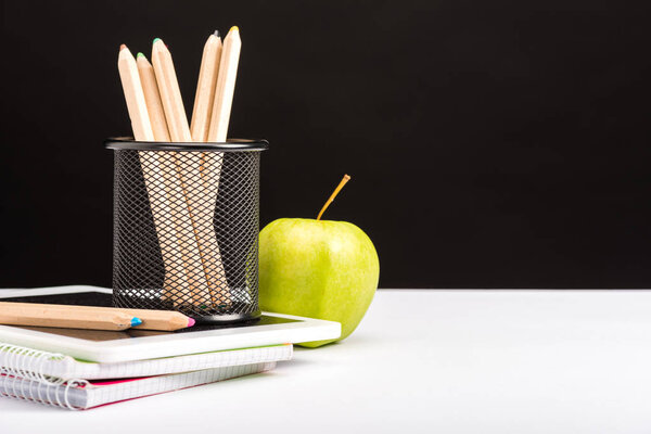 свежее яблоко, блокноты и карандаши изолированы на черном
