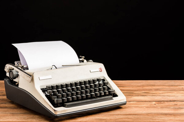 vintage typewriter with paper on wooden table isolated on black