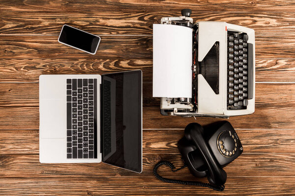 top view of typewriter, laptop, rotary dial telephone and smartphone on wooden table