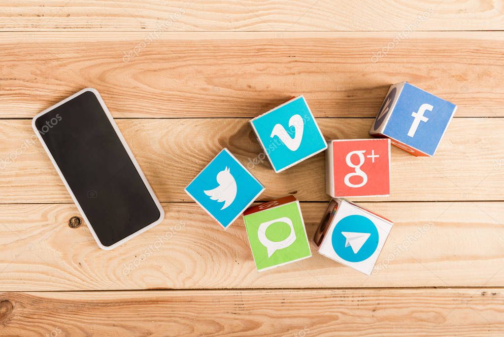 Top view of smartphone with blank screen and website icons on wooden background