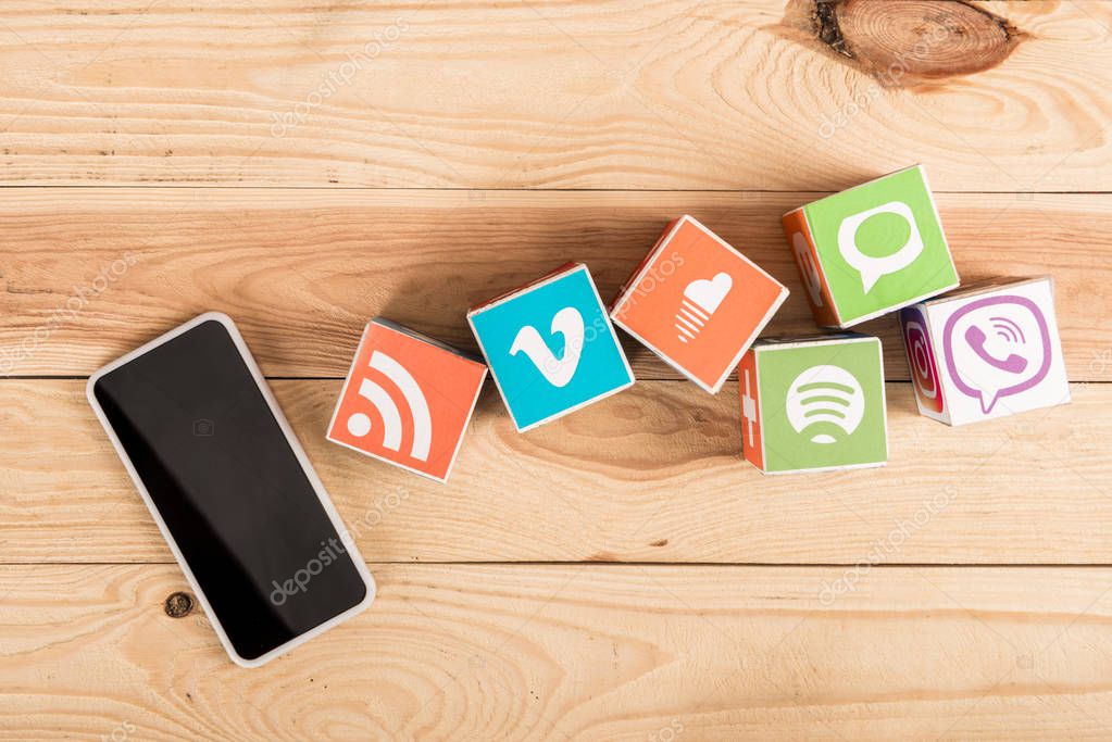 Top view of smartphone with blank screen and website icons on wooden background