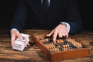 cropped shot of businessman holding russian rubles banknotes and using counting frame at wooden table clipart