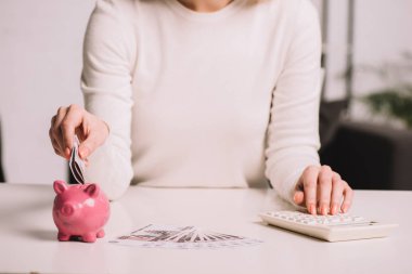 mid section of woman using calculator and putting russian rubles into piggy bank  clipart