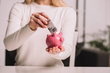 cropped shot of woman putting russian rubles into piggy bank, savings concept  clipart