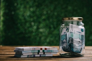 close-up view of glass jar with money and russian rubles banknotes on wooden table clipart