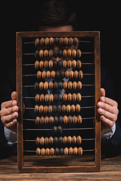 businessman holding abacus and looking at camera while sitting at wooden table