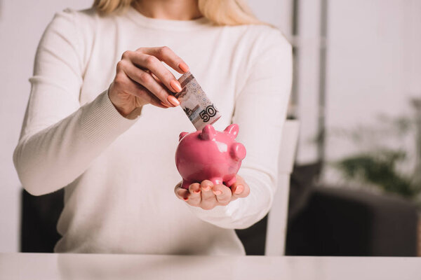 cropped shot of woman putting russian rubles into piggy bank, savings concept 