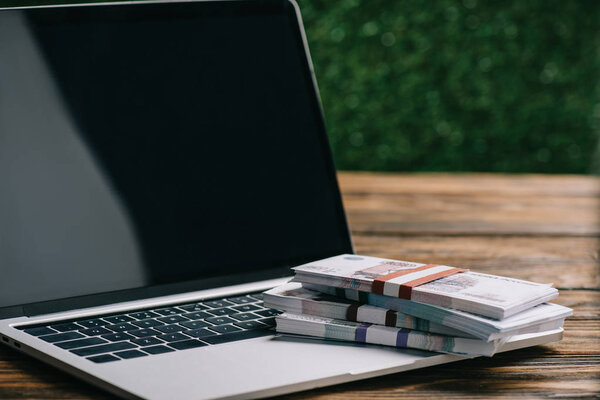 Крупный план ноутбука с чистым экраном и рублевыми банкнотами на деревянном столе
