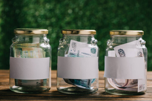 стеклянные банки с чистыми этикетками и банкноты российских рублей на деревянном столе
