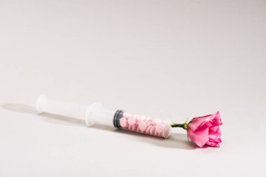 Studio shot of pink flower, syringe and pills on grey clipart