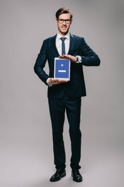 yakışıklı işadamı ekranda gri arka plan üzerinde dijital tablet facebook app ile tutarak 