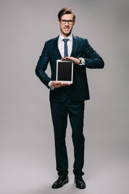 neşeli işadamı dijital tablet ile boş ekran gri arka plan üzerinde tutan 