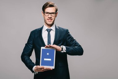 neşeli işadamı ekranda gri izole dijital tablet facebook app ile tutarak 