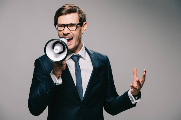 irritated businessman in suit screaming in megaphone on grey background